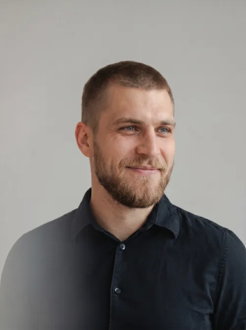 Made on Blogent: natural studio headshot of a man in a black shirt, soft grey backdrop, honest lighting, professional profile photo